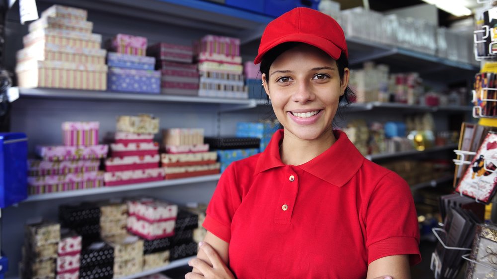 Woman wearing work uniform working in gift shop smiles