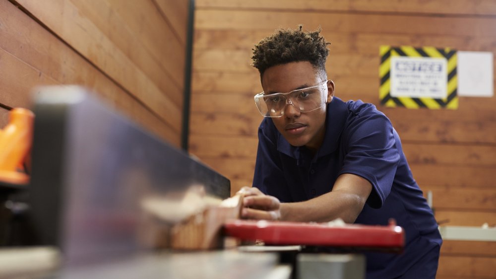 Boy with protective goggles cuts wood in workshop 